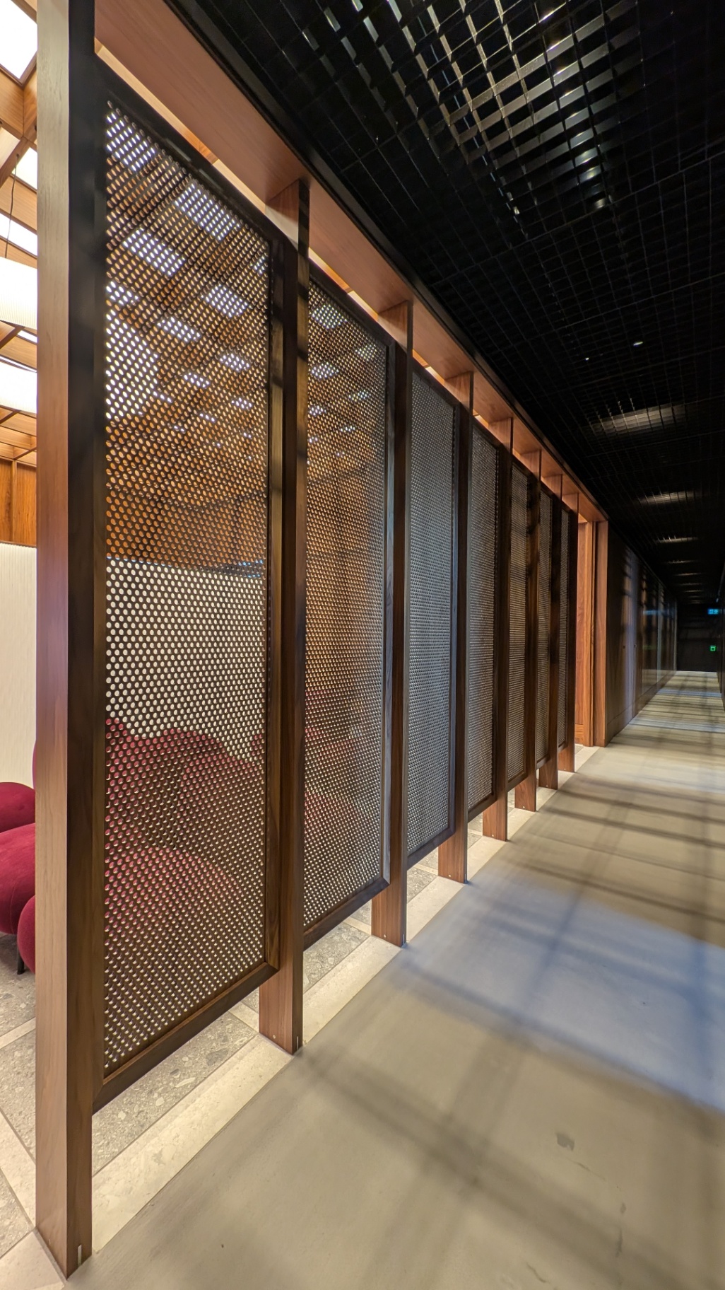Run of perforated walnut-framed screens lining a daylit corridor