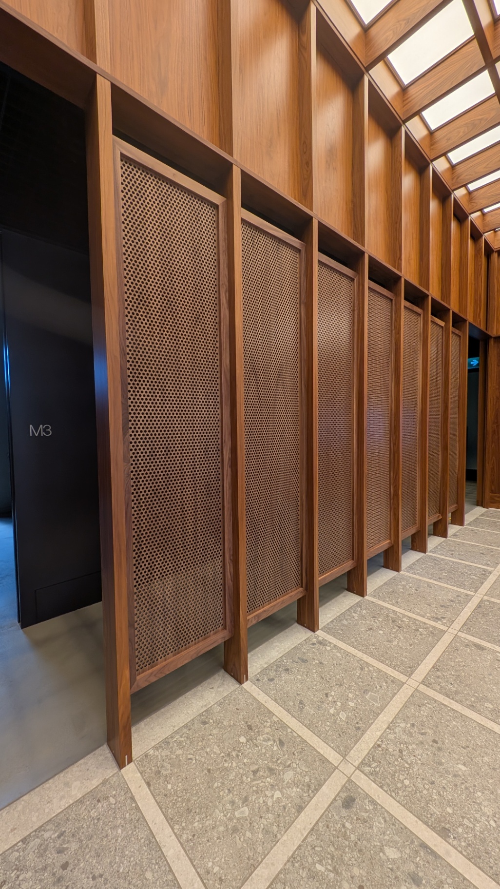 Custom walnut millwork wall with perforated infill panels along the M3 treatment wing