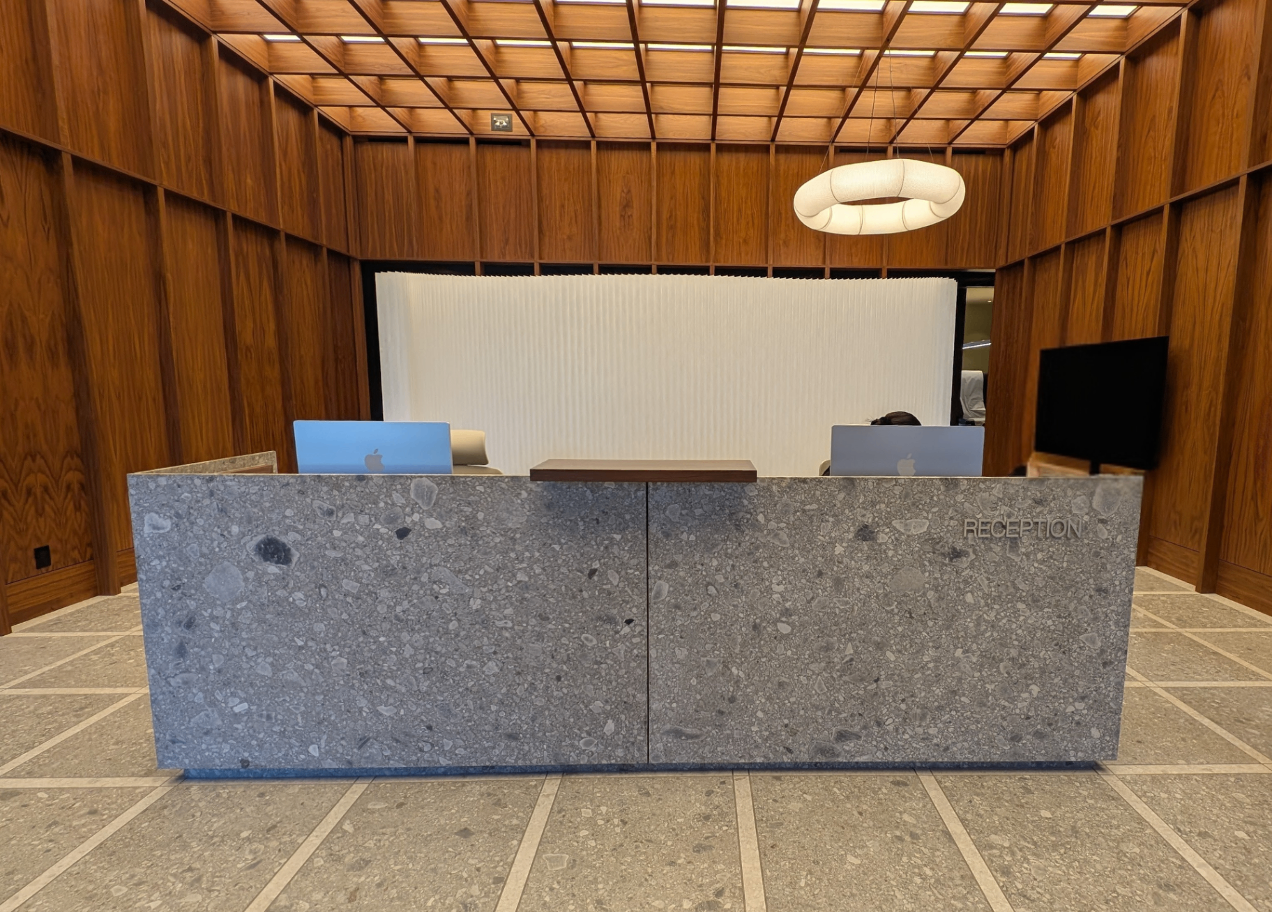 Surface Dermatology reception desk in honed terrazzo set against walnut paneled walls and a ring pendant
