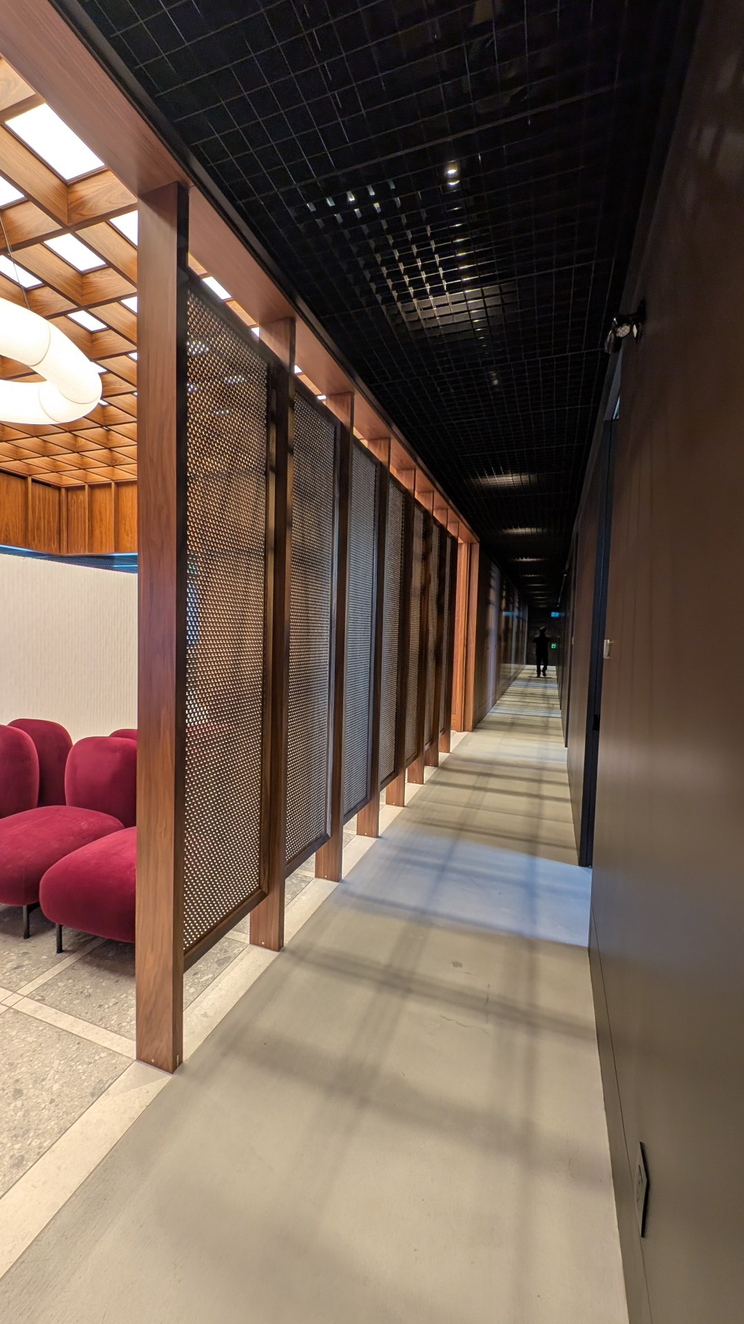 Treatment corridor framed by walnut posts, perforated metal screens, and a polished black ceiling